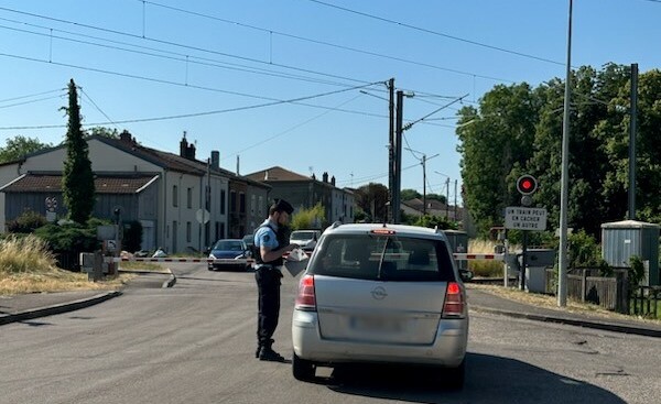 Un gendarme, vu de profil, dispense des conseils de pr&eacute;vention au conducteur d'un v&eacute;hicule gris arr&ecirc;t&eacute; &agrave; un passage &agrave; niveau, dont les barri&egrave;res sont baiss&eacute;es. Au second plan, plusieurs v&eacute;hicules attendent de l'autre c&ocirc;t&eacute; du passage &agrave; niveau.