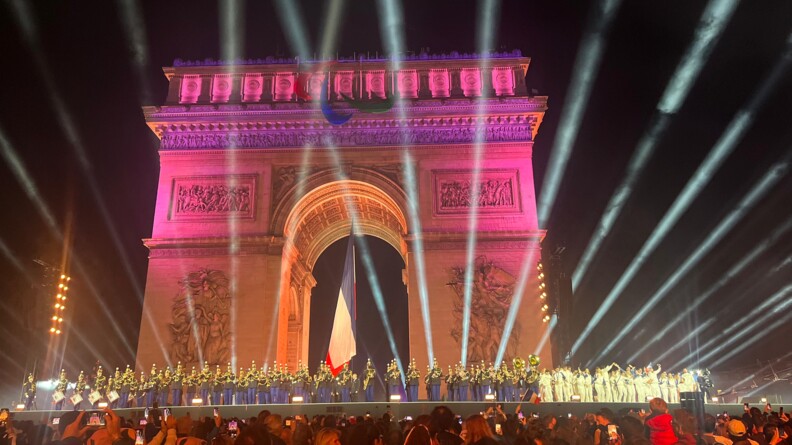 Sur une grande sc&egrave;ne install&eacute;e au pied de l'Arc de Triomphe, o&ugrave; flotte le drapeau fran&ccedil;ais, les musiciens de la Garde R&eacute;publicaine occupent les deux tiers de la sc&egrave;ne ; &agrave; droite, v&ecirc;tus de blanc, les athl&egrave;tes olympiques et paralympiques saluent la foule amass&eacute;e devant la sc&egrave;ne.
