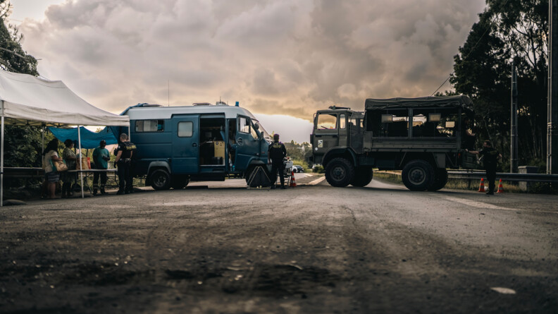 Vue sur un TRM et un Iribus gar&eacute;s en travers de la route. Sur la gauche, deux gendarmes mobiles, de dos, proc&egrave;dent au contr&ocirc;le d'identit&eacute; de trois pi&eacute;tons.