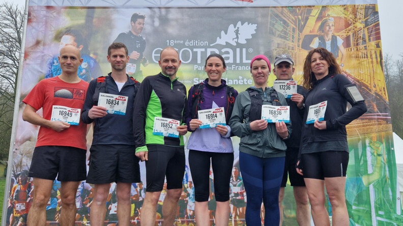 Agrandir l'image Sept sportifs devant un panneau de l'ecotrail de Paris, portant leur dossards devant eux