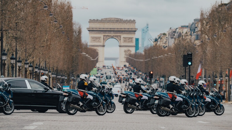 Des motards de la Garde républicaine précèdent une berline noire arborant le drapuea de l'ouzbékistan (bleu blanc et vert horizontal) sur les champs élysées