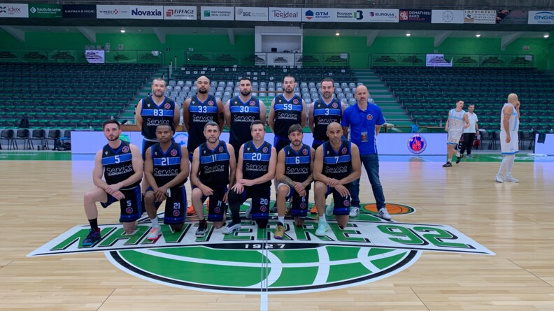 Les onze joueurs et l'entra&icirc;neur du Club sportif et de loisirs de la gendarmerie (CSLG) d&rsquo;Antibes Juan-les-Pins posent au centre du terrain de basket de la salle de Nanterre.