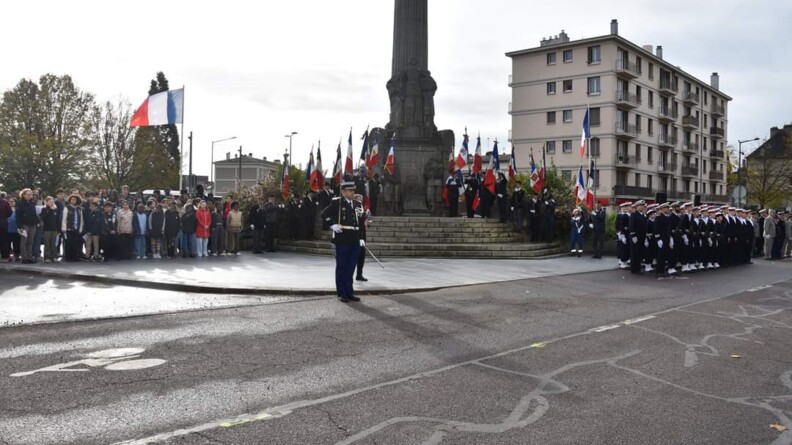 Agrandir l'image Des militaires et civils autour d'un monument aux morts orné de drapeaux