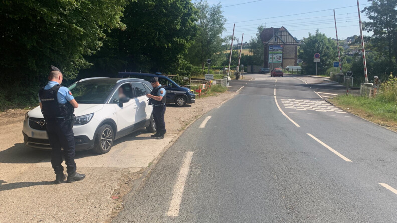 Un gendarme dispense des conseils de pr&eacute;vention &agrave; un conducteur arr&ecirc;t&eacute; sur le bas-c&ocirc;t&eacute;, &agrave; proximit&eacute; d'un passage &agrave; niveau, en arri&egrave;re-plan. Au premier plan, un second gendarme de dos.