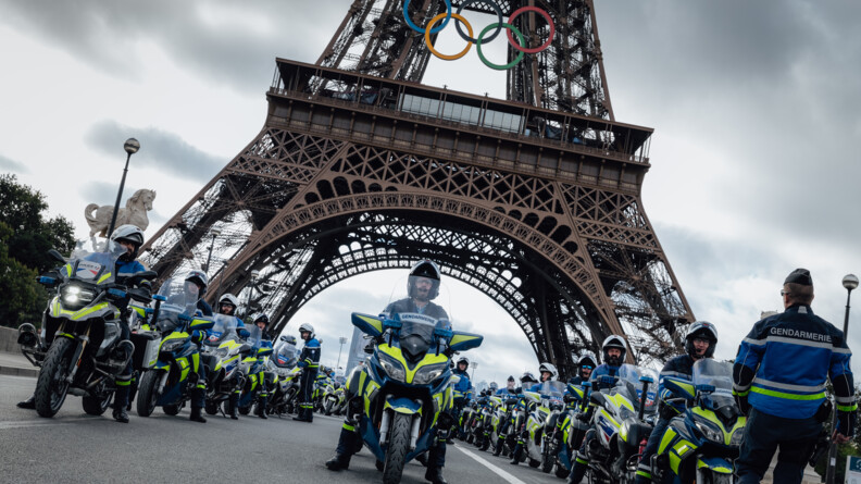 Des gendarmes motocylistes posent devant et sous la Tour Eiffel, assis sur leur véhicule.