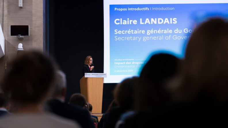 Photo de Claire Landais qui intervient lors d'un colloque. La secr&eacute;taire d'Etat du gouvernement s'exprime au micro devant l'assembl&eacute;e, debout derri&egrave;re un pupitre en bois.