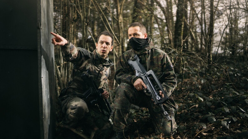 Deu gendarmes en treillis postés en forêt contre un mur en béton