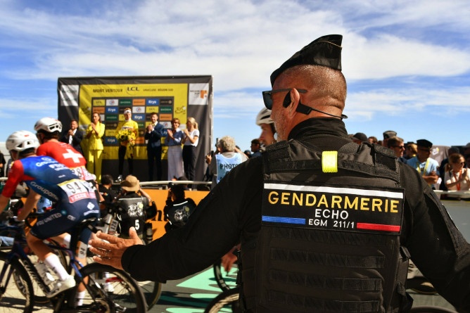 Photo d'un gendarme de dos, à l'arrivée du tour de France, au Mont Ventoux. Dans son dos est écrit GENDARMERIE ECHO EGM 211/1. On aperçoit le podium et les vanqueurs en aaarière plan.