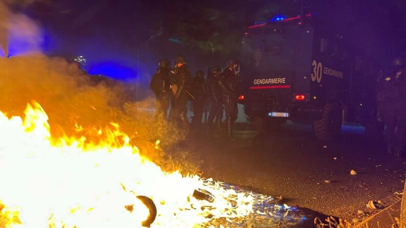 Un feu se propage au premier plan tandis que les gendarmes mobiles sont postés derrière un véhicule Centaure en arrière plan.