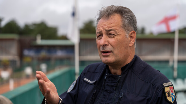 Un homme en tenue de gendarme discute debout face à nous