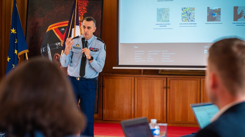Agrandir l'image Un gendarme s'exprime avec un micro devant une assemblée. Derrière lui, un grand écranr sur lequel est projetée sa présentation
