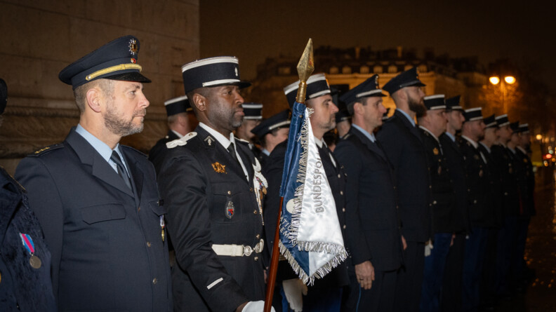 Des gendarmes fran&ccedil;ais et policiers allemands en rang dans la ville de nuit &eacute;clair&eacute;e. le premier gendarme vers la gauche tient dans sa main droite le fanion de l'unit&eacute;, bleu et blanc