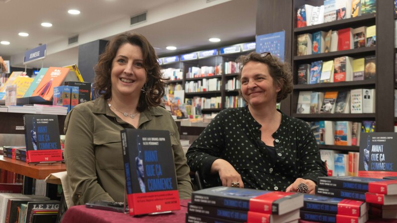 Agrandir l'image Au milieu des rayonnages d'une librairie, Marie-Laure Brunel-Dupin, à gauche, est assise au côté de Valérie Péronnet, derrière une table recouverte d'une nappe bordeaux, sur laquelle sont déposés plusieurs exemplaires de leur ouvrage : Avant que ça commence.