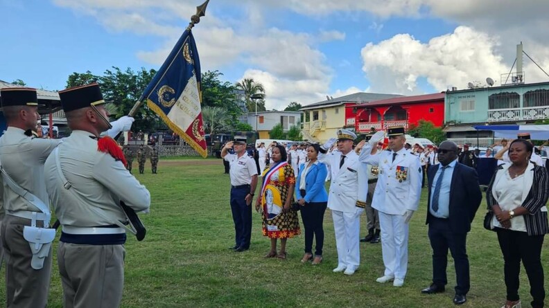 Les autorités militaires et civiles alignées sur une pelouse saluent le drapeau.