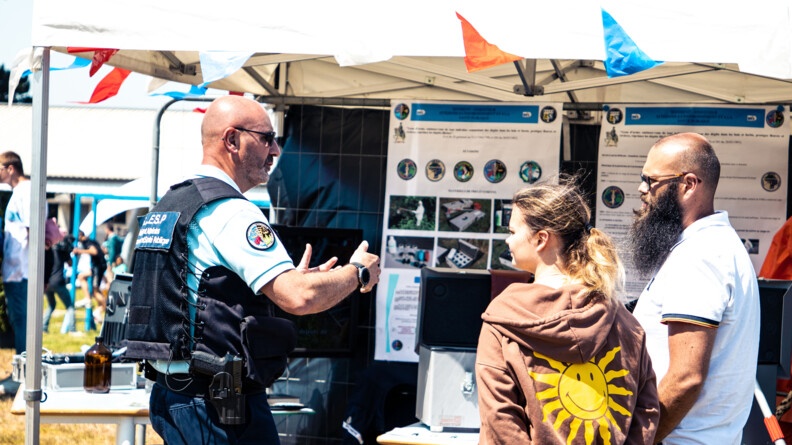 Un gendarme échange avec deux visiteurs devant un stand.