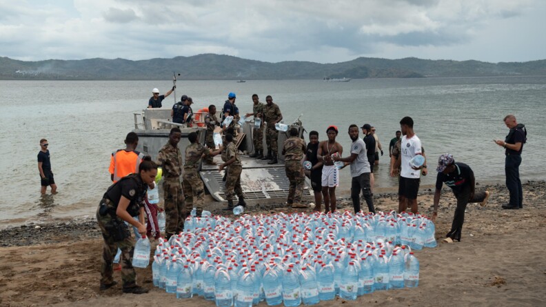 Des gendarmes, militaires et civils d&eacute;chargent des bidons d'eau d'une petit bateau sur la plage