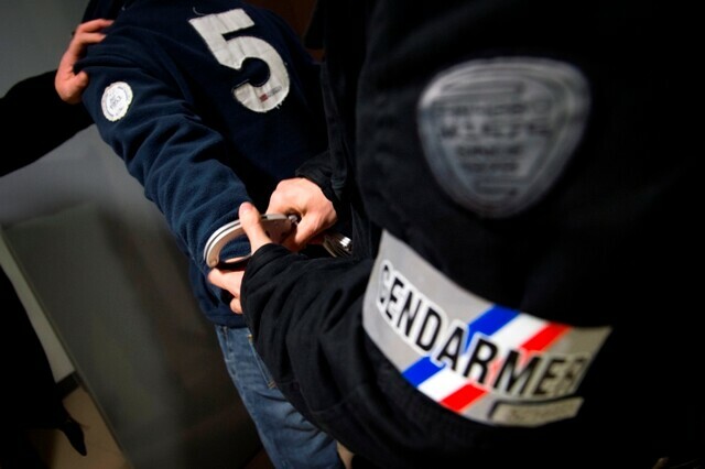 Un gendarme dont on ne voit que le brassard est entrain de menotter un individu.