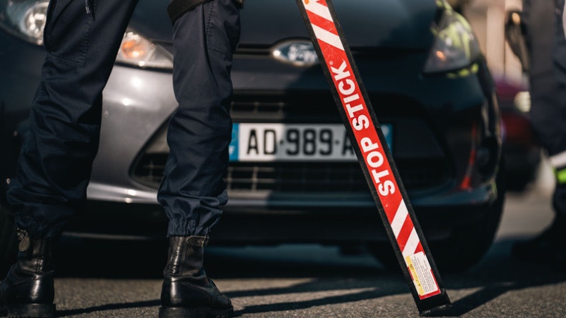 Agrandir l'image On aperçoit sur la photo les jambes d'un gendarme debout, face à un véhicule gris foncé, lors d'un contrôle routier, tenant un STOP STICK