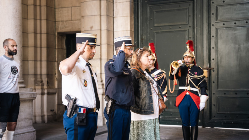Photo de coureurs, gendarmes, et garde r&eacute;publicain debout sous en porche. Les gendarmes effectuent un salut.