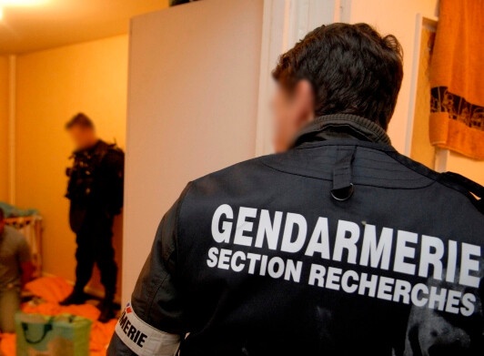 Agrandir l'image Enquêteur d'une section de recherches vu de dos. Au second plan un second gendarme surveille un individu interpellé à genou.