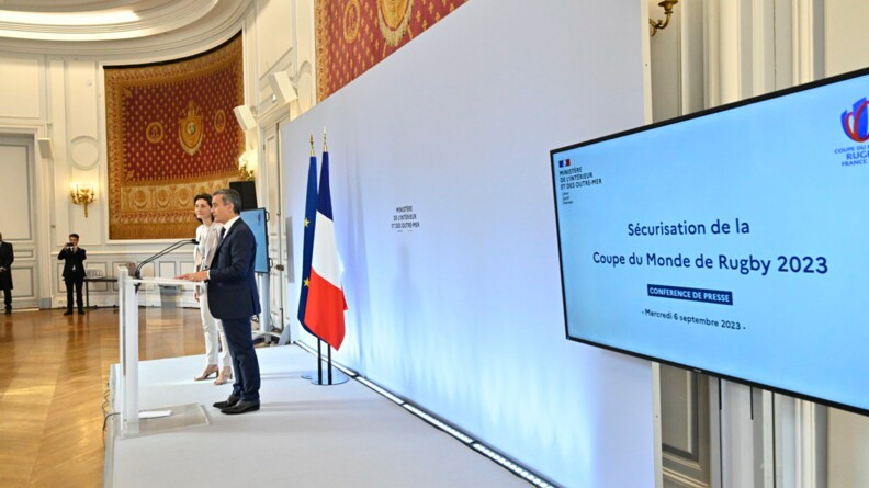 Le ministre de l'Intérieur, de profil, aux côtés de la ministre des Sports, derrière un pupitre. Au premier plan, un écran précisant le sujet de la conférence de presse : "Sécurisation de la coupe du Monde de rugby 2023"