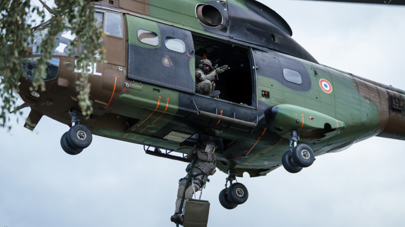 Un gendarme du GIGN descend en corde lisse depuis un Puma du GIH, tandis qu'un autre militaire embarqu&eacute;, arme en joue, l'appuie et s&eacute;curise sa descente.