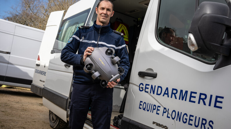 Agrandir l'image Une gendarme tenant un appprail devant un véhicule blanc siglé "Gendarmerie équipe plongeurs"