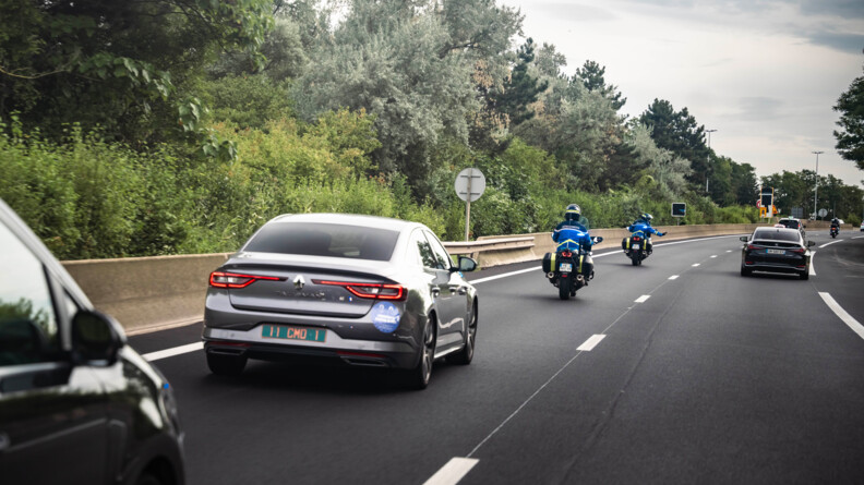 Motocyclistes escortant un convoi et faisant signe à un véhicule de s'écarter.