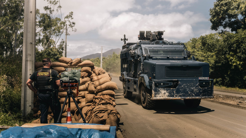 Un gendarme mobile vu de dos, derri&egrave;re un mur de sacs de sable. Devant lui, sur la route, un Centaure.