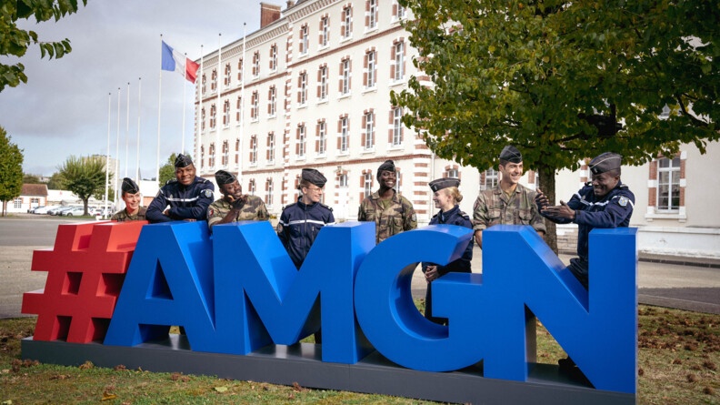 Agrandir l'image Huit élèves de l'Académie militaire de la gendarmerie nationale, quatre des pays amis de la France et quatre français, posent devant l'Académie, derrière le logo bleu et rouge.