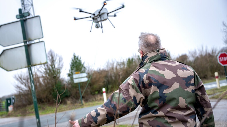 Photo d'un gendarme réserviste de la Section Opérationnelle de Lutte contre la cyber-menace (SOLC). Il est de dos et fait un pousse pour diriger son collègue qui manoeuvre un drone filaire.