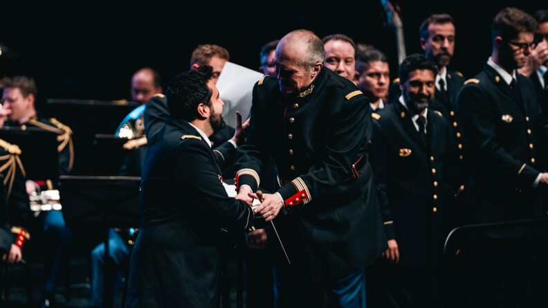 un membre des choeurs de l'armée françasie et un che d'orchestre de la garde se serrent joyeusement les mains devant les musiciens de l'orchestre de la garde républicaine