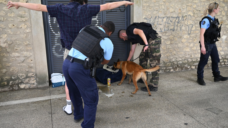 La photo représente des gendarmes, accompagnés d'un malinois, fouillant le sac d'un festivalier,  à l'occasion du festival Garorock. L'un des gendarmes fouille le festivalier, un homme, se tenantn debout, de dos, les bras levés afin de faciliter la fouille.