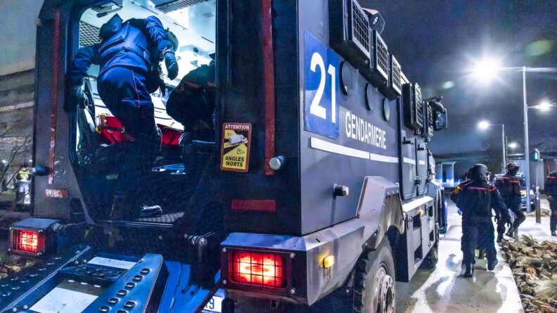 Vue sur l'arrière ouvert d'un véhicule blindé Centaure, à l'intérieur duquel les pompiers du groupe d'extraction s'affairent. Sur la droite d'autres pompiers progressent.