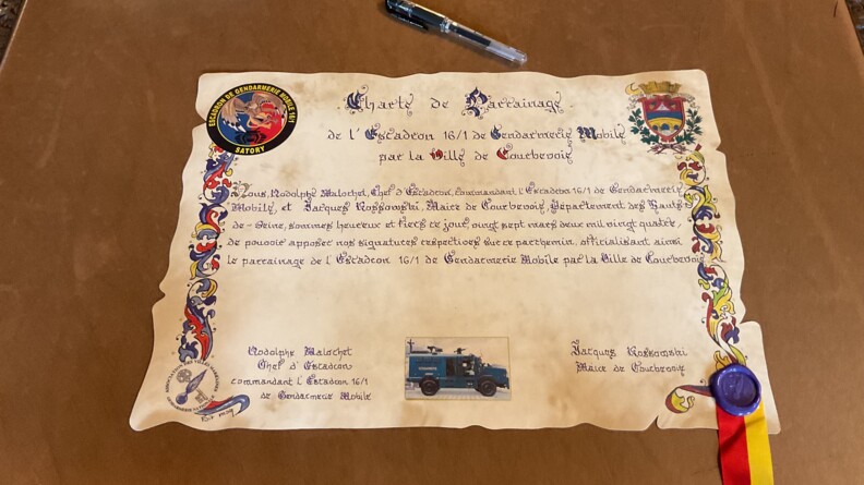 Charte de parrainage de l’Escadron de gendarmerie mobile (EGM) 16/1, unité du groupement blindé de gendarmerie mobile de Versailles-Satory, par la ville de Courbevoie, posée sur un bureau.