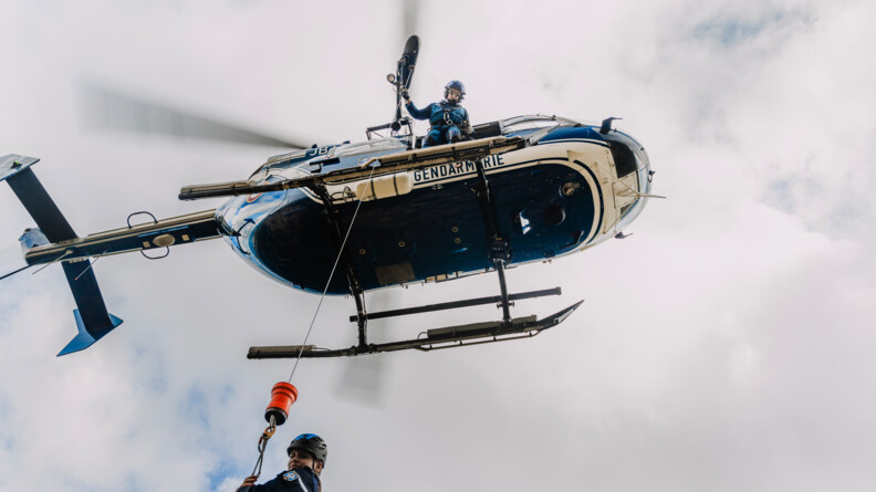 vue en contre plongée proche, d'un gendarme tenant un câble, en cours d'hélitreuillage, une gendarme étant hélitreuillée