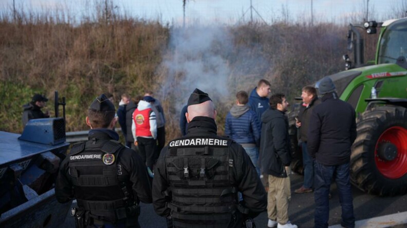 Deux gendarmes mobiles de dos. En fond devant eux, des agricutleurs échangent calmement.