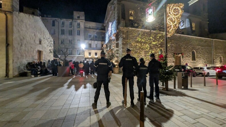 Quatre gendarmes de dos devant la foule dans une ville décorée pour Noël