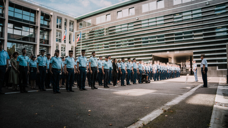 Dans la cour carrée au pied d'un bâtiment, des gendarmes alignés au garde-à-vous
