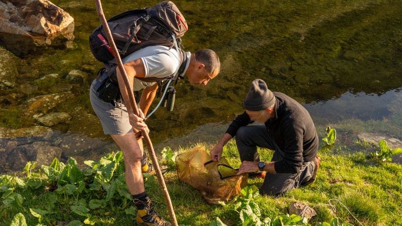 Agrandir l'image Un agent de l'OFB contrôle la nasse d'un pêcheur au bord d'un lac. La photo est prise de jour en extérieur.