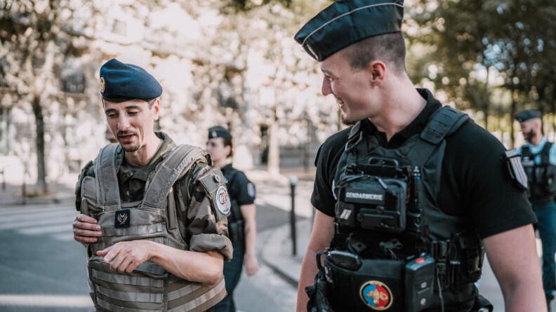 Un aumônier musulman en treillis échange avec un gendarme mobile dans la rue, tous deux sont souriants