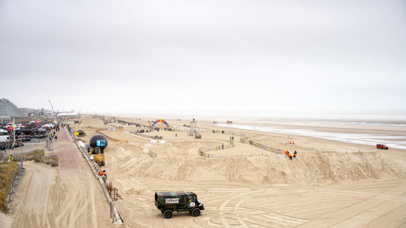 Agrandir l'image Photo du circuit de course de sable depuis les dunes. On y voit des gens, des camions. Sur la gauche on voit aussi des quads garés en attendant le début de la course.