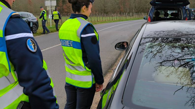 Agrandir l'image Deux gendarmes de dos contrôlant un véhicule sur le bord de la route. Au loin, deux autres gendarmes font de même.