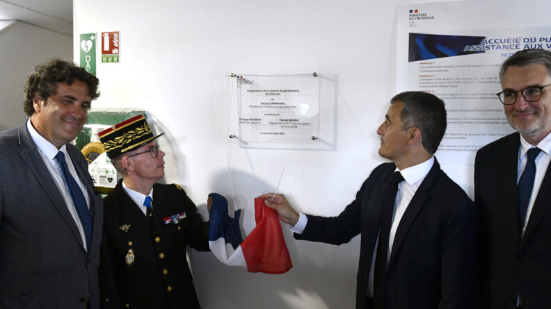 Le g&eacute;n&eacute;ral de corps d'arm&eacute;e Andr&eacute; Petillot et le ministre de l'Int&eacute;rieur et des Outre-mer, G&eacute;rald Darmanin, encadr&eacute;s par deux hommes en civil vus de face, d&eacute;voilent la plaque de la nouvelle caserne de gendarmerie de Libourne.