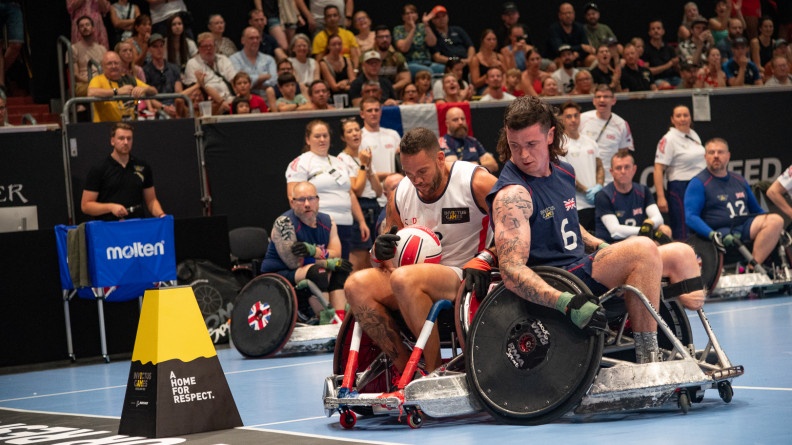 Duel entre deux athlètes sur un terrain de basket fauteuil sous les yeux des spectateurs dans les gradins.