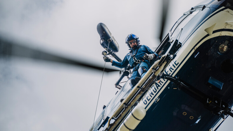 vue en contre plongée proche, d'un gendarme tenant un câble, en cours d'hélitreuillage
