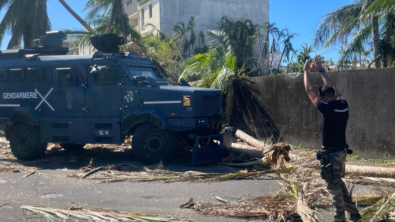 Agrandir l'image Un gendarme guide un véhicule blindé de la gendarmerie, déblayant une route bloquée par des branches et des troncs d'arbres arrachés, après le passage du cyclone Garance à La Réunion.