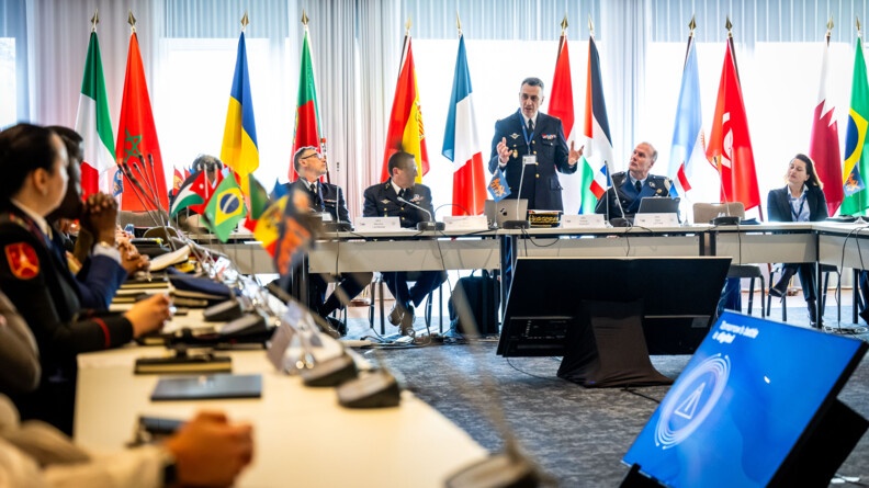 Agrandir l'image Autour d'une table avec de très nombreux drapeaux, un homme, un général de gendarmerie français est en train de parler devant d'autres officiers.