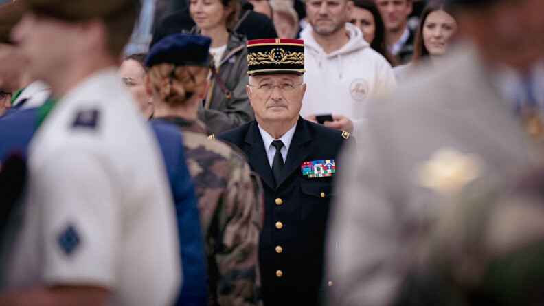 Le directeur général de la gendarmerie nationale se tient debout au milieu d'une foule. Face à lui se tient une femme militaire que l'on aperçoit de dos.