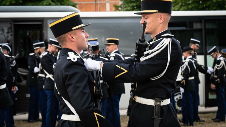 Agrandir l'image Deux élèves-gendarmes en vareuse avec leur FAMAS ajustent leur tenue pour les répétitions du défilé
